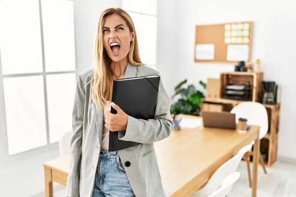 Blonde business woman at the office angry and mad screaming frustrated and furious, shouting with anger. rage and aggressive concept.