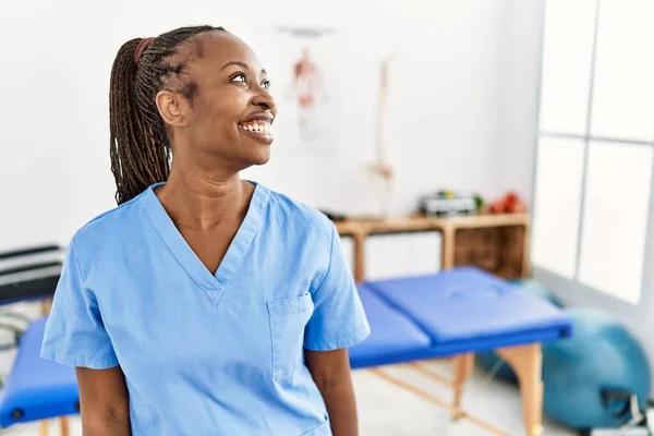 Black woman with braids working at pain recovery clinic looking away to side with smile on face, natural expression. laughing confident.