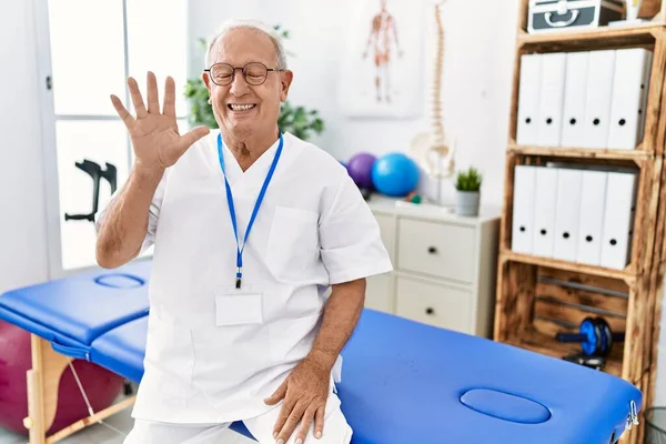 在疼痛康复诊所工作的资深理疗人员带着自信和快乐的笑容 用五号手指显示和指点 — 图库照片