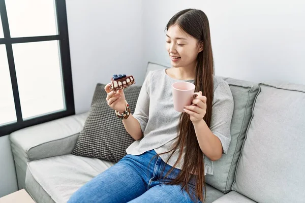 Young Asian Woman Eating Pastries Sitting Sofa Living Room — Stockfoto