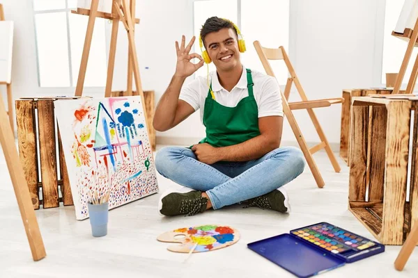 Young hispanic man at art studio smiling positive doing ok sign with hand and fingers. successful expression.