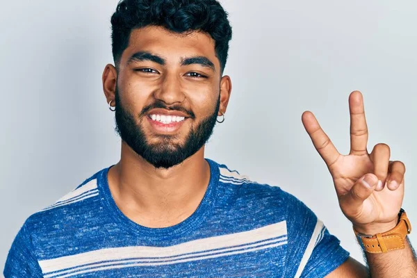 Sakallı, sıradan çizgili tişörtlü, gülümseyen, kameraya göz kırpan ve zafer işareti yapan bir Arap. İki numara.. 