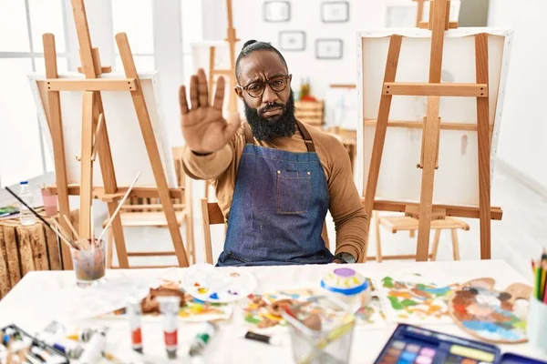 African american artist man at art studio doing stop sing with palm of the hand. warning expression with negative and serious gesture on the face.