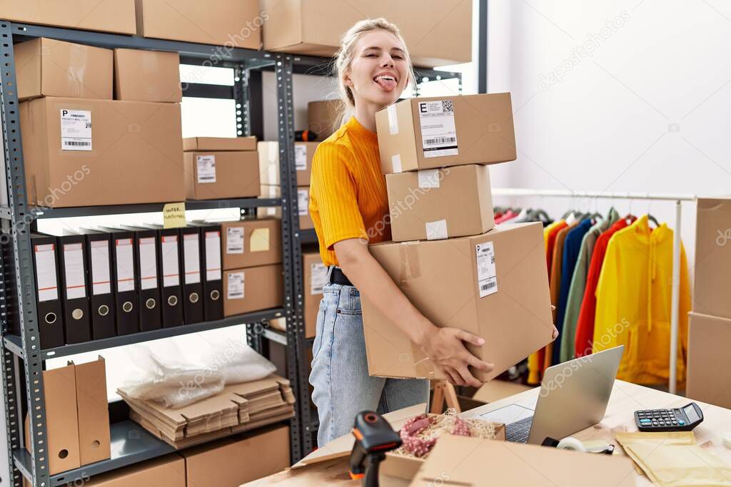 Young blonde woman working at small business ecommerce sticking tongue out happy with funny expression. 