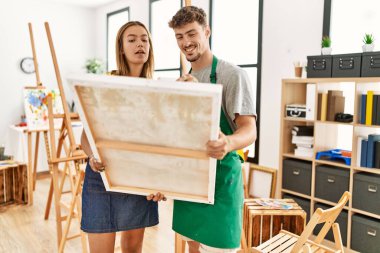 Genç İspanyol sanatçı çift resim stüdyosunda tuval tutarken mutlu gülümsüyor..