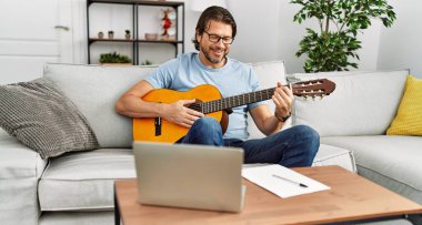 Orta yaşlı beyaz bir adam evde klasik gitar çalıyor.