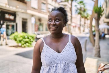 Genç Afrikalı Amerikalı kadın gülümseyerek şehirde mutlu mesut duruyor..