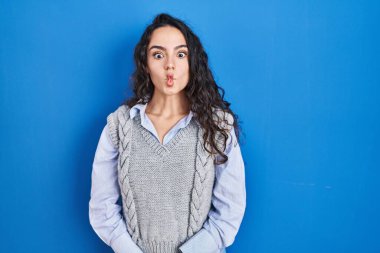 Mavi arka planda duran genç esmer kadın dudaklarıyla balık suratı yapıyor, çılgınca ve komik bir jest. Komik ifade. 