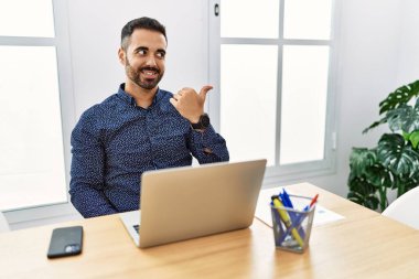 Ofiste sakallı, mutlu yüzüyle gülümseyen ve baş parmağıyla yüzünü gösteren genç bir İspanyol.. 