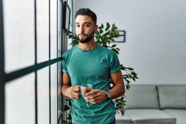 Genç Arap adam evde çay içerek kendinden emin gülümsüyor.