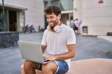 Sokakta dizüstü bilgisayar kullanarak gülümseyen İspanyol genç adam.