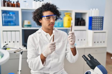 Laboratuvarda test tüpleri tutan bilim adamı üniforması giyen İspanyol bir genç.