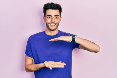 Gündelik tişört giyen, elleri büyük ve büyük boy işareti gösteren İspanyol bir genç. Ölçü sembolü. Kameraya bakıp gülümsüyor. ölçüm kavramı. 