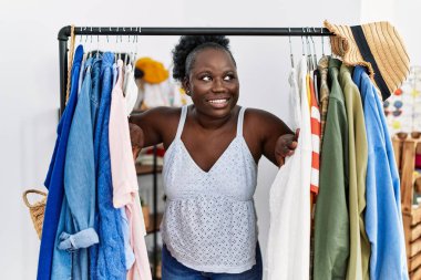 Young african american woman customer appearing throw clothes rack at clothing store
