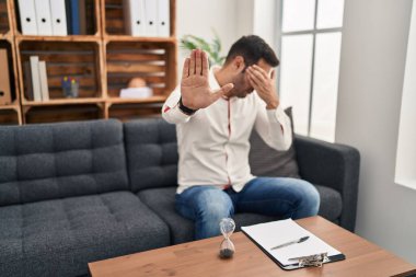 Danışma ofisinde çalışan, sakallı, elleriyle gözlerini kapatan üzgün ve korku ifadesiyle jestleri durduran genç bir İspanyol. utangaç ve olumsuz kavram. 