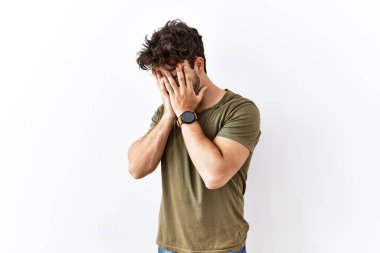 Hispanic man standing over isolated white background with sad expression covering face with hands while crying. depression concept. 