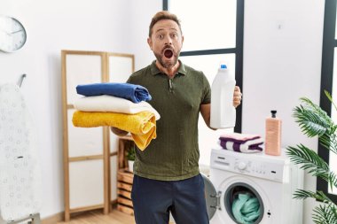 Orta yaşlı bir adam elinde temiz çamaşır ve deterjan şişesiyle çılgınlığı kutluyor ve başarıya hayret ediyor gözleri açık heyecanla bağırıyor.. 