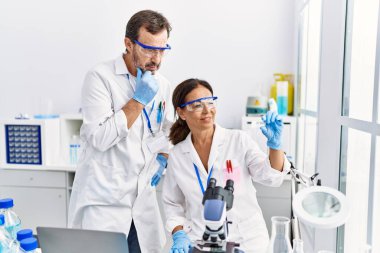 Bilim adamı üniforması giyen orta yaşlı erkek ve kadın ortaklar laboratuarda örnek analiz ediyorlar.