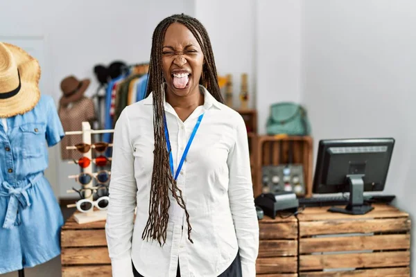 Black woman with braids working as manager at retail boutique sticking tongue out happy with funny expression. emotion concept.