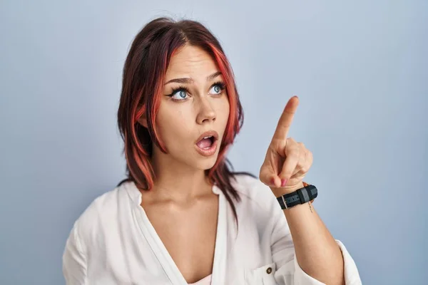 Young caucasian woman wearing casual white shirt over isolated background pointing with finger surprised ahead, open mouth amazed expression, something on the front