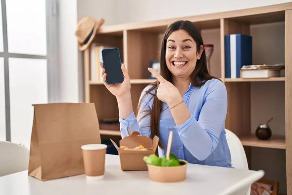 若いですブルネット女性食べる取ります食べ物にホームショースマートフォンの画面笑顔幸せなポインティングとともに手と指 — ストック写真