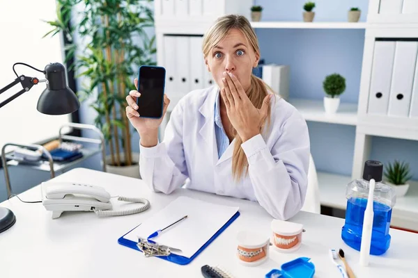 Красивая Стоматолог Женщина Показывает Смартфон Покрывающий Рот Рукой Шокирован Боится — стоковое фото