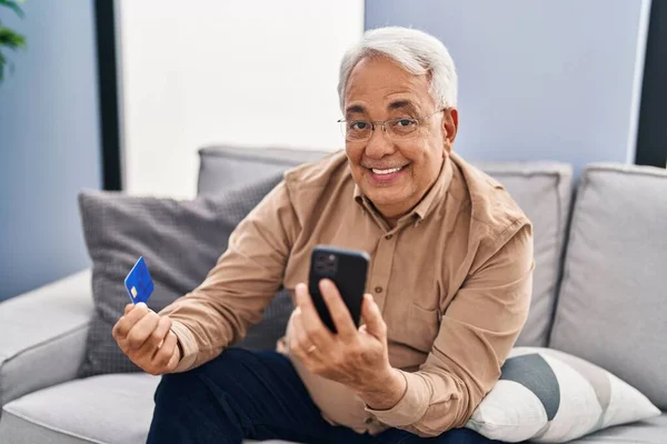 Senior man using smartphone and credit card sitting on sofa at home