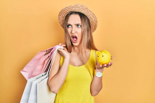 Young Blonde Girl Holding Shopping Bags Piggy Bank Angry Mad — Stock Photo, Image