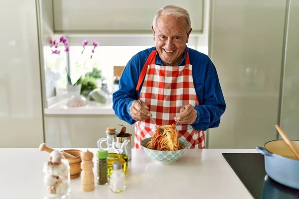 老人面带微笑 自信地把番茄酱和意大利面混合在厨房里 — 图库照片