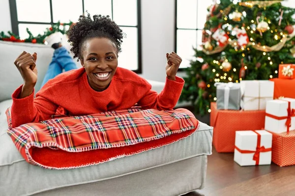 アフリカ系アメリカ人の若い女性が腕の筋肉を誇りに笑顔を示すクリスマスツリーでソファの上に横たわっていた フィットネスのコンセプト — ストック写真