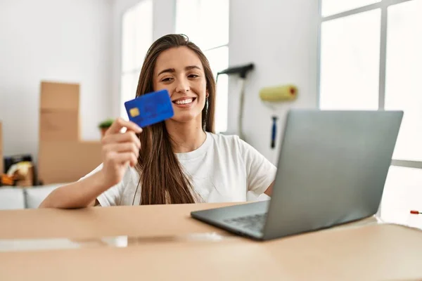 年轻的惊慌失措的女人带着自信的笑容在新家使用信用卡和笔记本电脑 — 图库照片