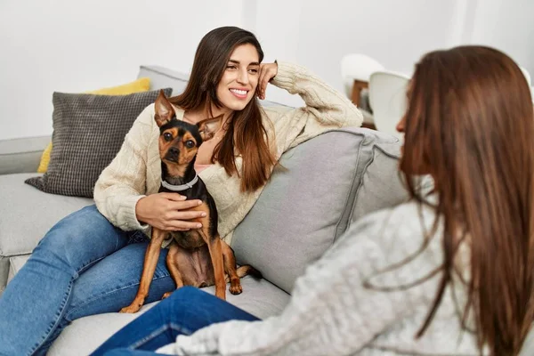 Two women smiling confident sitting on sofa with dog at home