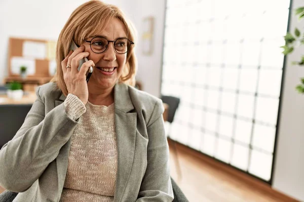Middle age businesswoman smiling happy talking on the smartphone at the office.