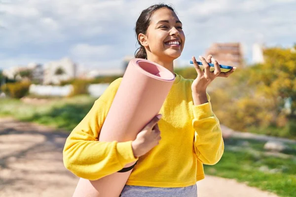 Genç Afrikalı Amerikalı kadın parkta yoga minderiyle akıllı telefondan konuşuyor.