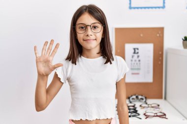 Young hispanic girl wearing glasses showing and pointing up with fingers number five while smiling confident and happy. 