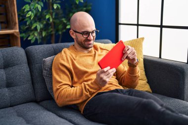 Evdeki kanepede oturan dokunmatik ped kullanan genç adam.