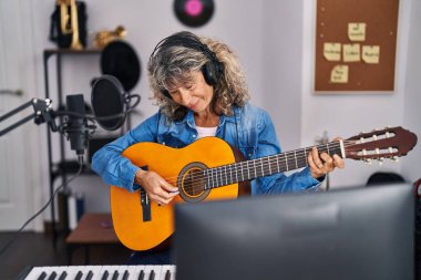 Müzik stüdyosunda gitar çalan orta yaşlı bir kadın şarkıcı.