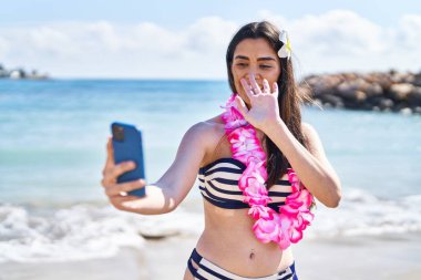 Bikini giyen genç İspanyol kadın deniz kenarında akıllı telefonla selfie çekiyor.