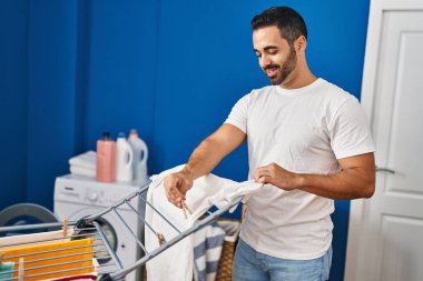 Genç İspanyol adam gülümsüyor. Çamaşır odasında kendine güveni tam bir elbise asıyor.