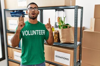 Genç Hintli gönüllü bağış kutusunu tutuyor. Şaşırmış ve şaşırmış bir şekilde yukarı bakıyor ve parmaklarıyla işaret ediyor ve kollarını kaldırıyor.. 