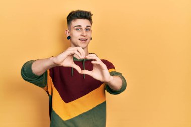 Kulakları genişlemiş, sıradan bir kazak giymiş, aşkla gülümseyen, elleriyle kalp sembolü yapan beyaz bir çocuk. romantik kavram. 