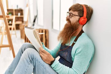 Young redhead man listening to music and drawing at art studio