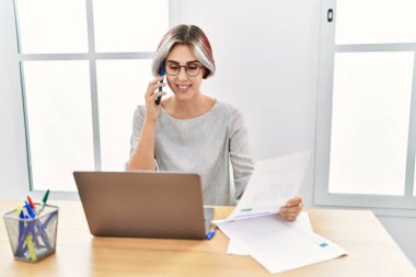 Genç beyaz iş kadını ofiste çalışan akıllı telefondan konuşuyor..