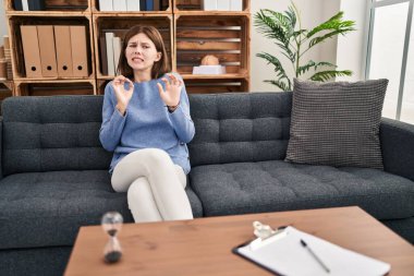 Young brunette woman at consultation office disgusted expression, displeased and fearful doing disgust face because aversion reaction. with hands raised 