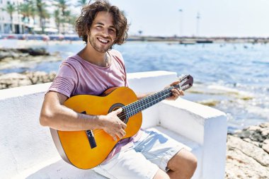 Genç İspanyol adam klasik gitar çalıyor sahildeki bankta oturuyor..
