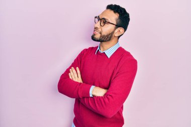 Sakallı, iş gömleği ve gözlüklü, kolları çapraz ve kendinden emin bir şekilde yana bakan İspanyol bir adam. 