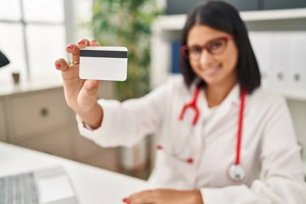 Young latin woman wearing doctor uniform holding credit card at clinic