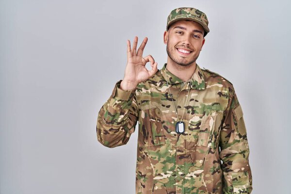 Young hispanic man wearing camouflage army uniform smiling positive doing ok sign with hand and fingers. successful expression. 