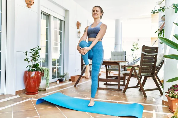 Güzel bir beyaz kadın evindeki terasta antrenman yapıyor ve esniyor. Asya 'da ve sağlıkta yoga minderinde çalışıyorum..