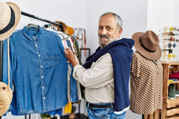 Kıdemli gri saçlı adam elbise mağazasında akıllı telefon kullanarak fotoğraf çekiyor.